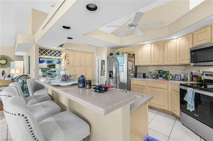 Kitchen with stainless steel appliances, light wood finish cabinetry, a breakfast bar, light tile patterned flooring, and a tray ceiling