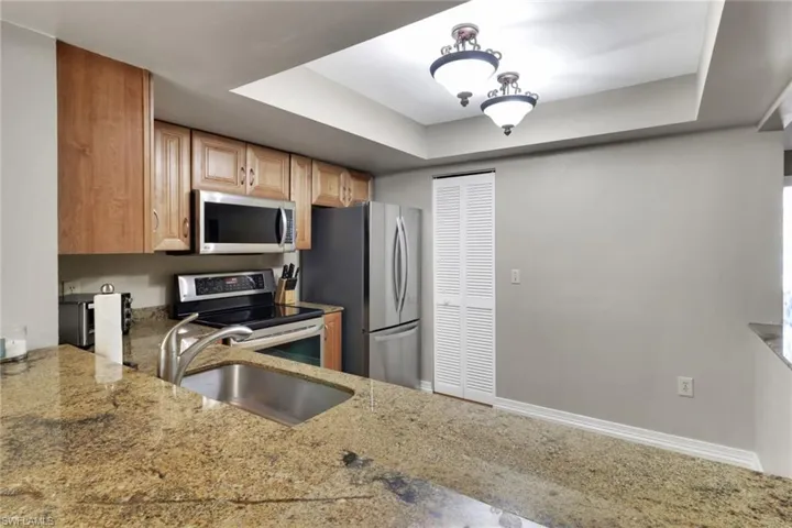 Kitchen featuring a tray ceiling, appliances with stainless steel finishes, and light stone counters