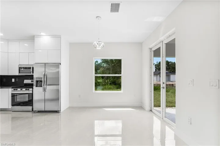 Kitchen with decorative light fixtures, appliances with stainless steel finishes, a wealth of natural light, and white cabinetry
