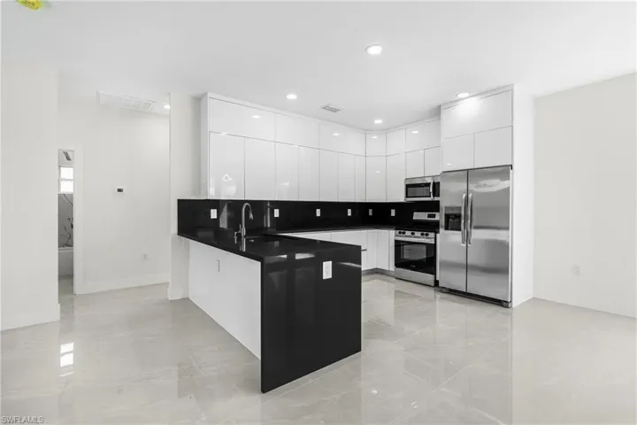 Kitchen with sink, kitchen peninsula, white cabinetry, appliances with stainless steel finishes, and decorative backsplash