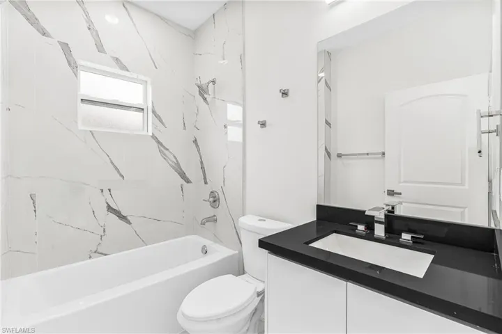 Full bathroom with vanity, tiled shower / bath combo, and toilet