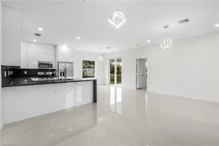 Kitchen with white cabinets, appliances with stainless steel finishes, hanging light fixtures, and sink