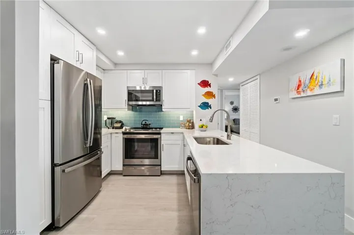 Kitchen with appliances with stainless steel finishes, light stone countertops, a peninsula, white cabinets, and backsplash