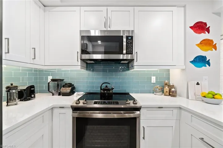 Kitchen with stainless steel appliances, white cabinets, and light stone counters