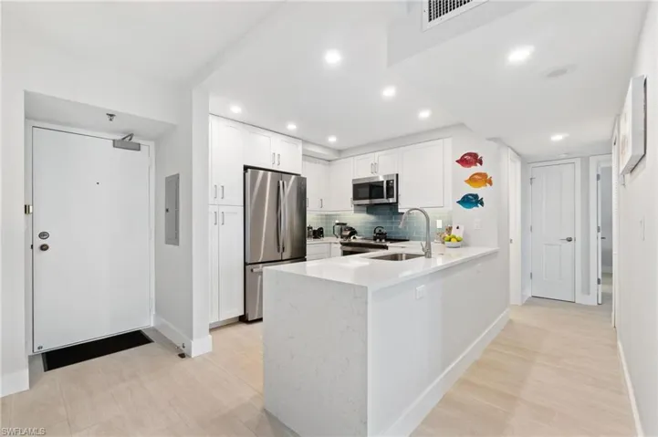 Kitchen featuring light stone counters, white cabinets, appliances with stainless steel finishes, a peninsula, and backsplash
