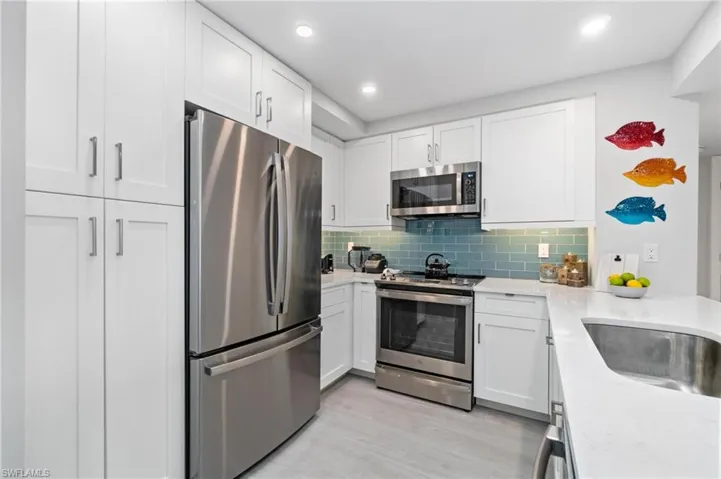 Kitchen featuring appliances with stainless steel finishes, white cabinets, light stone countertops, decorative backsplash, and light wood-type flooring