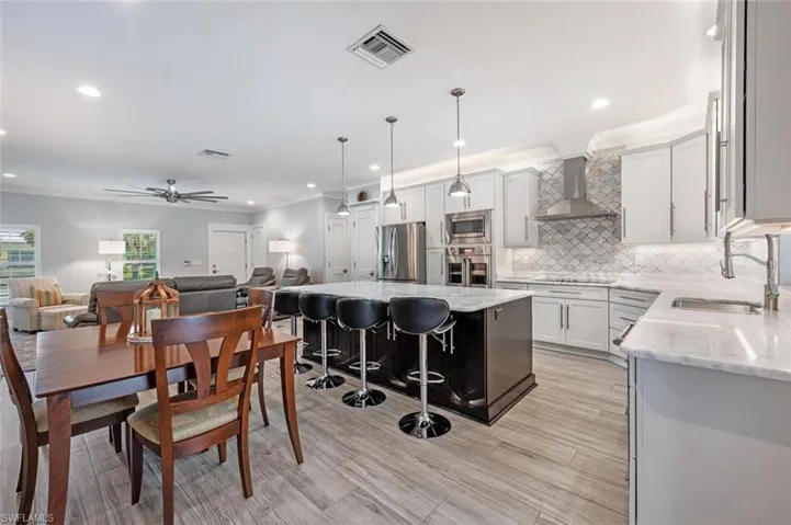Kitchen with wall chimney range hood, appliances with stainless steel finishes, open floor plan, recessed lighting, and backsplash