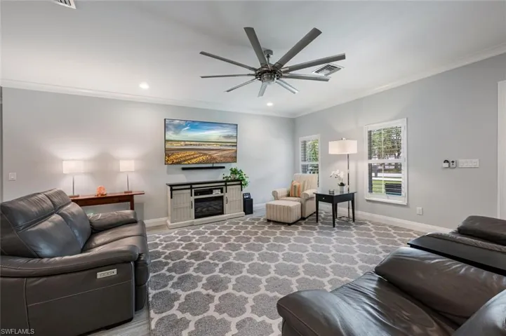 Living area featuring crown molding, ceiling fan, a glass covered fireplace, and recessed lighting