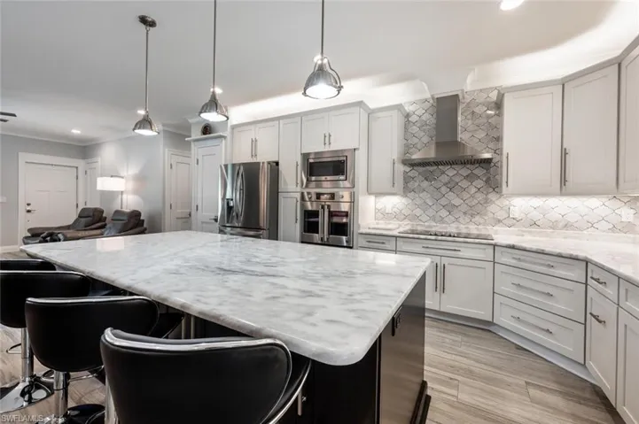 Kitchen with appliances with stainless steel finishes, wall chimney range hood, ornamental molding, a center island, and tasteful backsplash