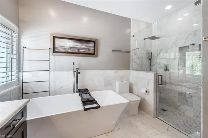 Bathroom featuring healthy amount of natural light, a freestanding bath, tile walls, a marble finish shower, and marble finish floors