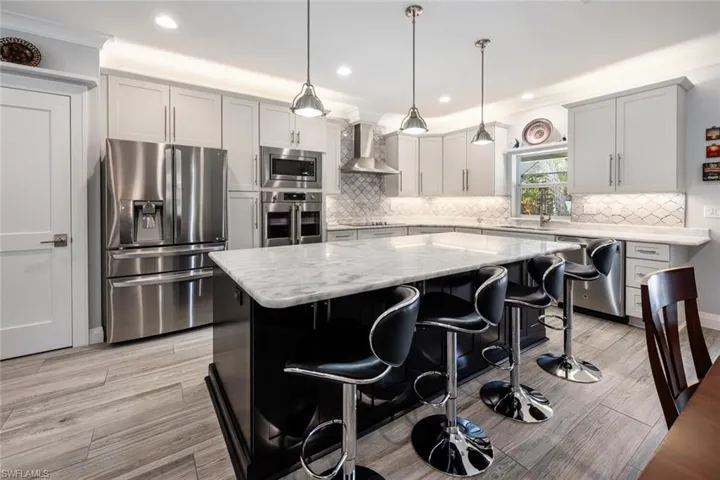 Kitchen featuring appliances with stainless steel finishes, wall chimney exhaust hood, a center island, tasteful backsplash, and recessed lighting