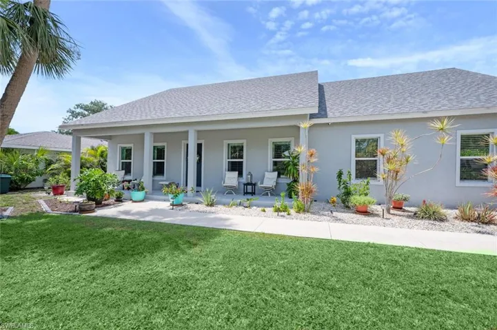Rear view of house with roof with shingles, covered porch, stucco siding, and a lawn