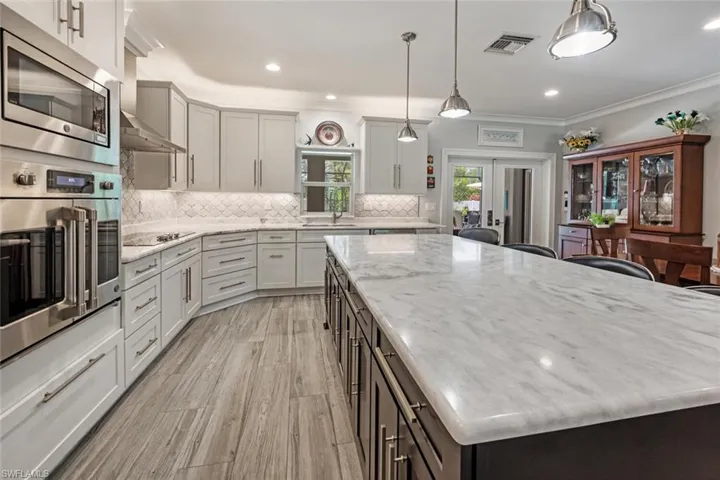 Kitchen with stainless steel appliances, a kitchen island, tasteful backsplash, light stone countertops, and crown molding