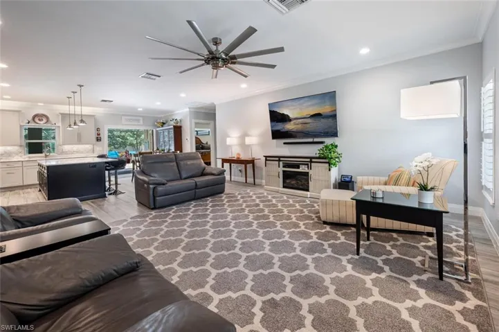 Living area featuring crown molding, light wood-style floors, ceiling fan, recessed lighting, and a glass covered fireplace