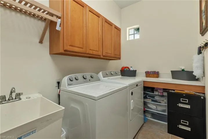 Laundry room with washer and clothes dryer, cabinets, light tile patterned floors, and sink