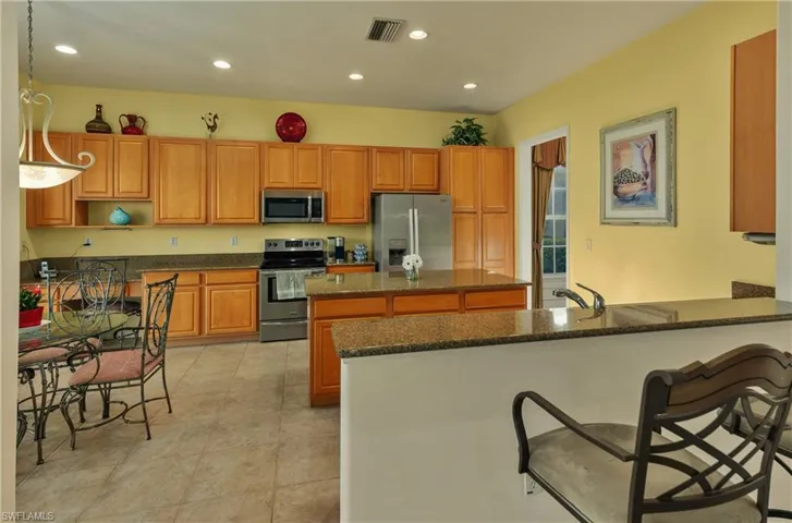 Kitchen featuring kitchen peninsula, appliances with stainless steel finishes, a kitchen bar, dark stone countertops, and hanging light fixtures