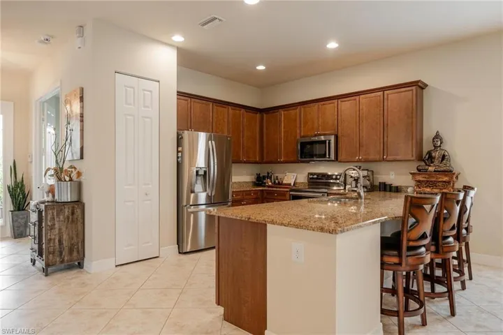 Kitchen featuring stainless steel appliances, stone countertops, a kitchen bar, sink, and light tile floors