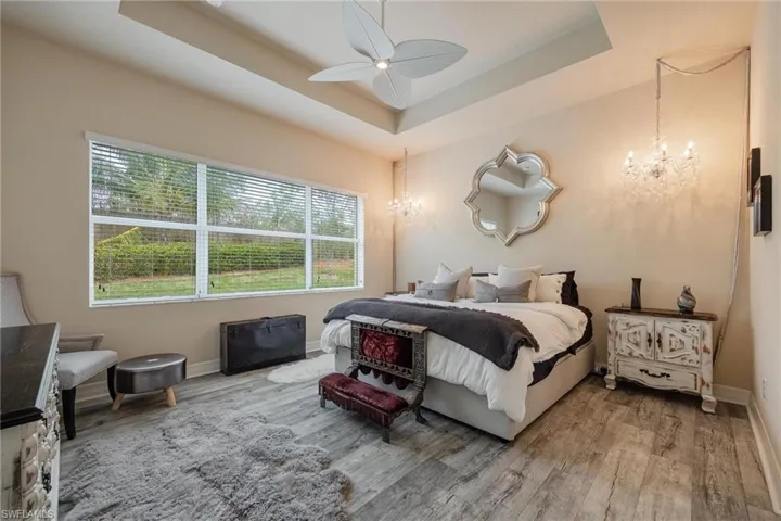 Bedroom with a tray ceiling, wood-type flooring, and ceiling fan with notable chandelier