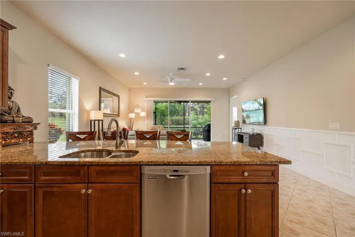 Kitchen featuring ceiling fan, light stone counters, sink, dishwasher, and light tile floors