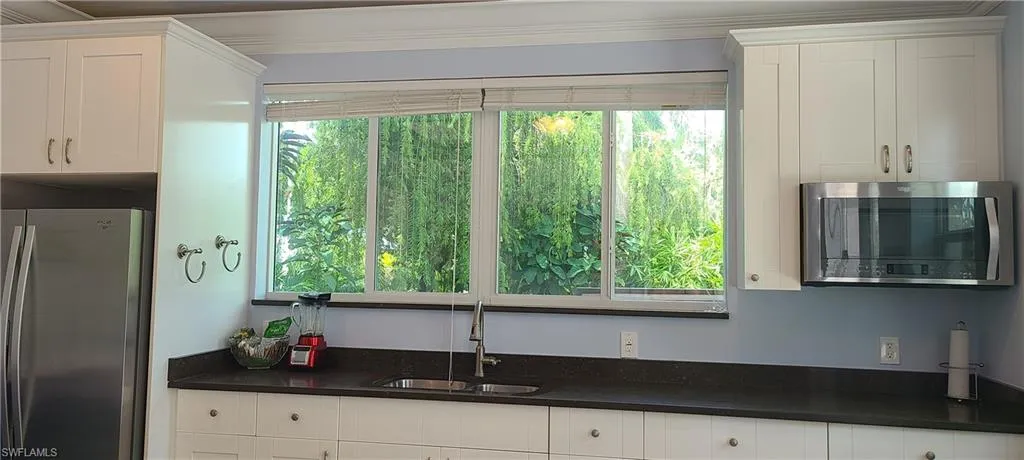 Kitchen featuring healthy amount of natural light, stainless steel appliances, white cabinetry, and crown molding