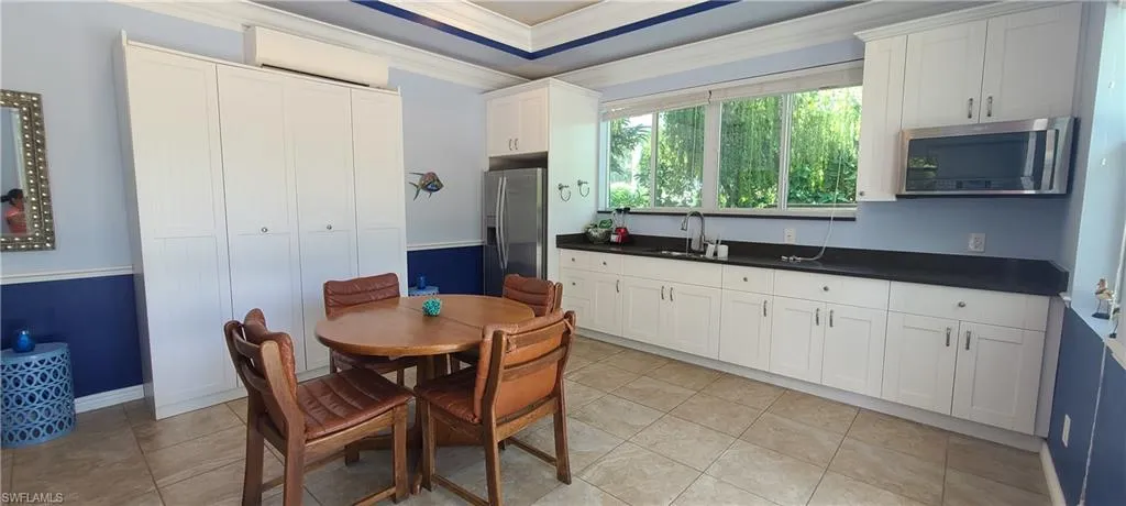 Kitchen with dark countertops, ornamental molding, white cabinets, appliances with stainless steel finishes, and a wall mounted air conditioner