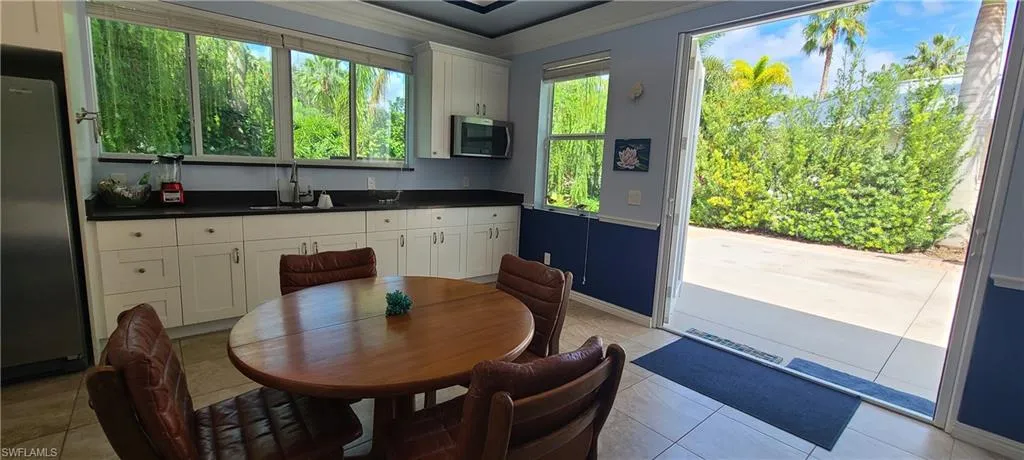 Kitchen featuring dark countertops, white cabinets, appliances with stainless steel finishes, ornamental molding, and light tile patterned floors