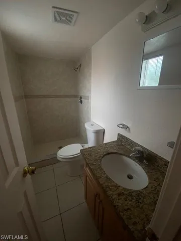 Bathroom featuring tiled shower, vanity, tile patterned floors, and toilet