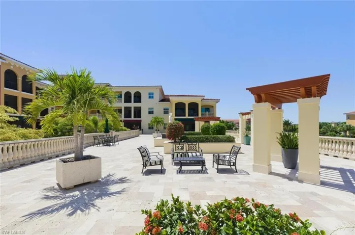 Expansive outdoor courtyard featuring light-toned paver flooring, a decorative balustrade wall, and mature landscaping