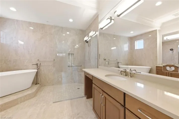 Spacious bathroom featuring a freestanding soaking tub, a walk-in shower with clear glass enclosure, and a double vanity with an integrated sink and light-toned countertop