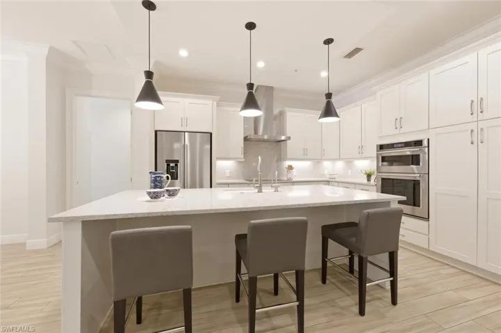 Spacious kitchen featuring a large central island with a light-toned countertop, white shaker-style cabinetry, stainless steel appliances, and pendant lighting fixtures
