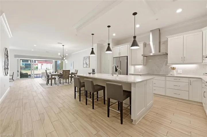 Modern kitchen featuring white shaker cabinetry, stainless steel appliances, a large center island with pendant lighting, and wood-finish flooring