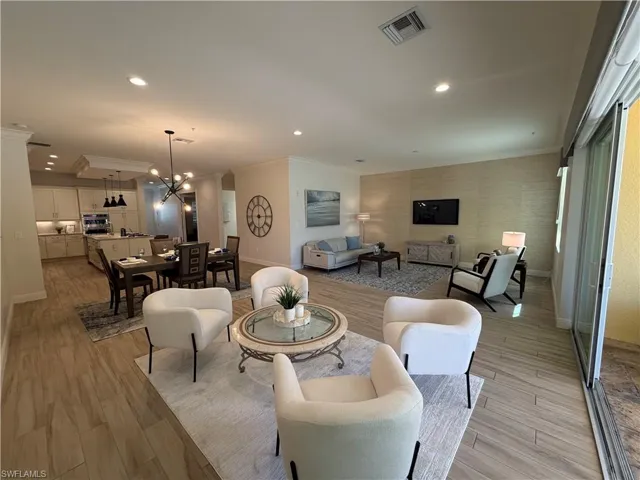 Living room featuring crown molding, light wood-style flooring, suspended lighting, and an accent wall