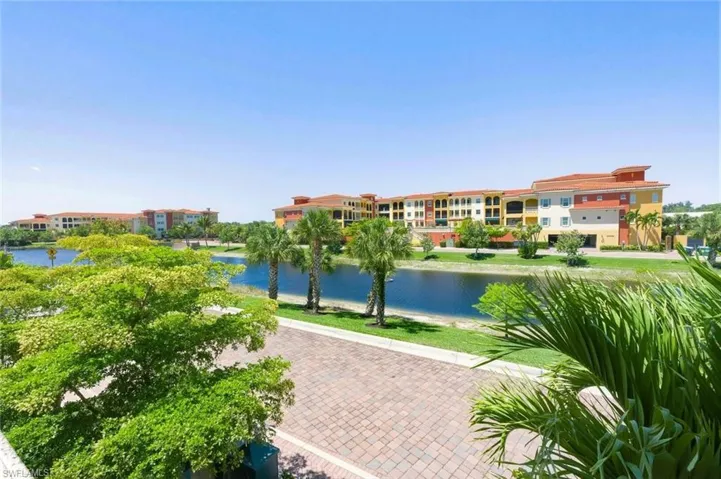Waterfront setting featuring a paved street, lush green landscaping, and mature palm trees