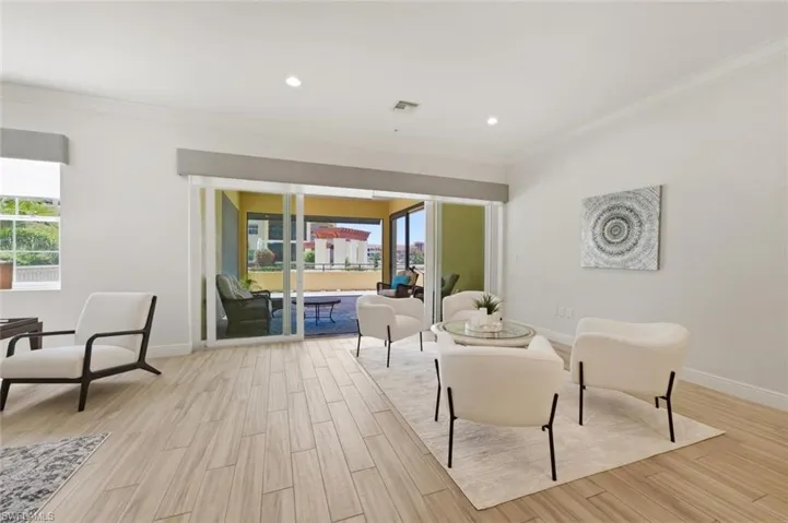 Spacious living area featuring light wood-finish flooring, recessed lighting, crown molding, and large sliding glass doors leading to an outdoor patio