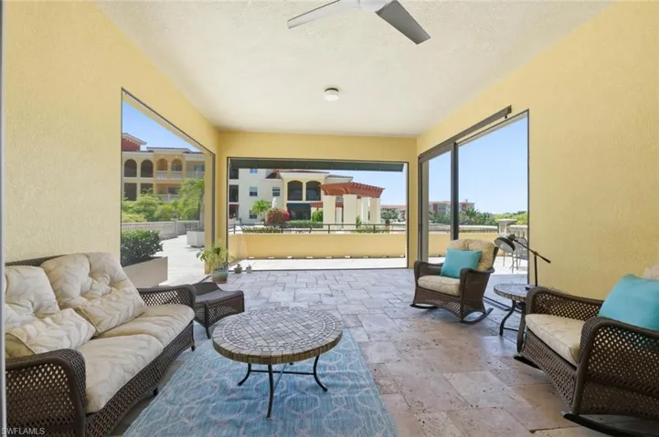 Expansive outdoor patio featuring stone tile flooring, a ceiling fan, and large openings to the exterior