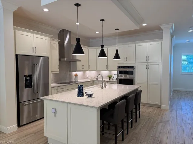 Kitchen with crown molding, stainless steel appliances, white cabinetry, a kitchen breakfast bar, and light stone counters
