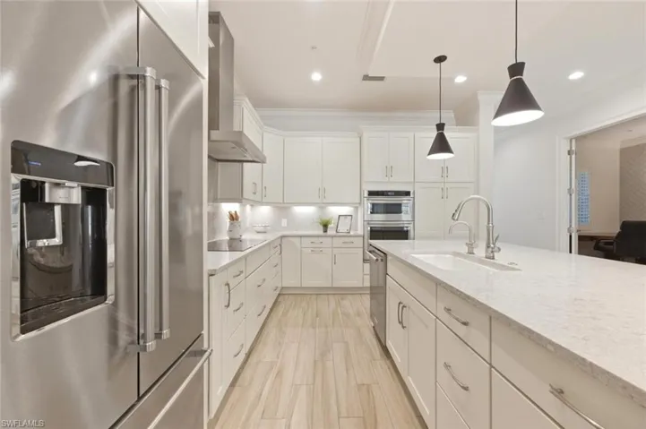 Kitchen featuring a large stainless steel refrigerator, white cabinetry, integrated stainless steel appliances, a center island with a sink, and wood-finish flooring