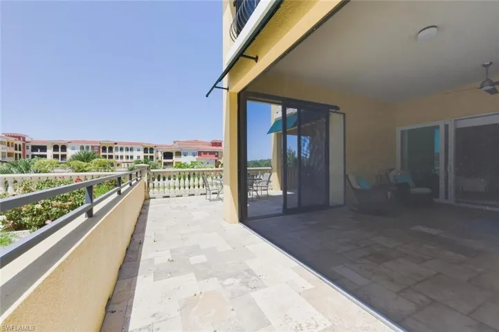 Expansive outdoor patio and balcony featuring stone tile flooring, baluster railing, and an awning over the sliding glass doors