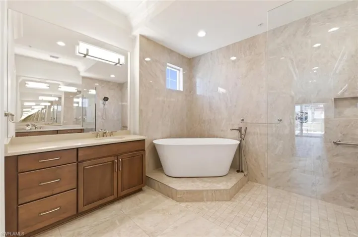 Expansive bathroom featuring a freestanding soaking tub, a large walk-in shower with a glass enclosure, a vanity with wood cabinetry and an integrated sink, full-height wall tiling, and recessed lighting