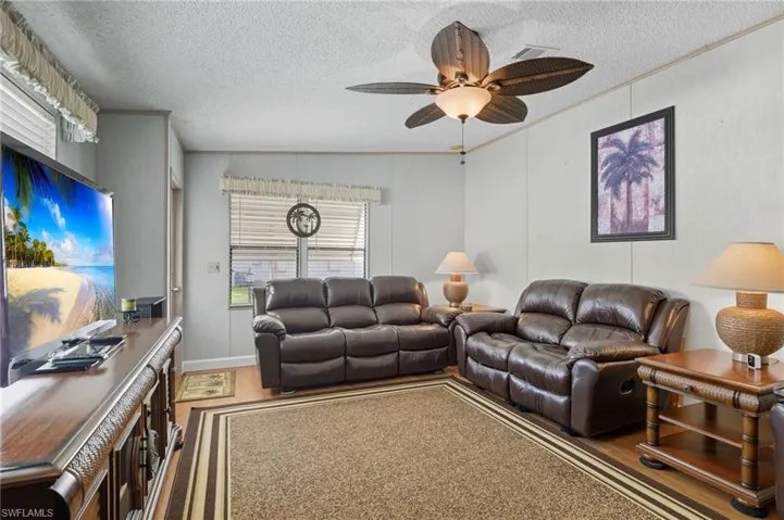 Living room with ornamental molding, a textured ceiling, wood finished floors, and a ceiling fan