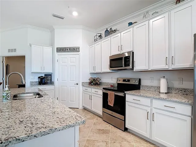 Kitchen featuring stainless steel appliances, light stone countertops, white cabinetry, and ornamental molding
