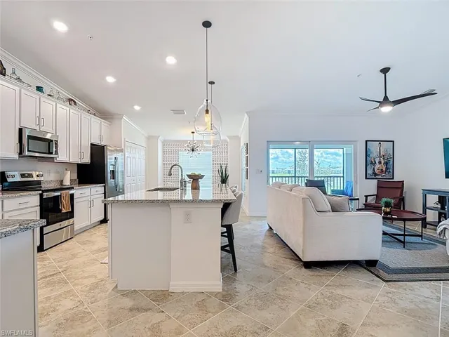 Kitchen featuring stainless steel appliances, ornamental molding, a breakfast bar, an island with sink, and hanging light fixtures