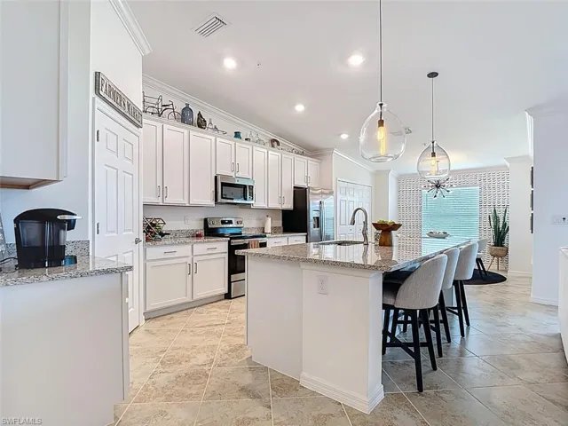 Kitchen with light stone countertops, a center island with sink, a breakfast bar, ornamental molding, and decorative light fixtures
