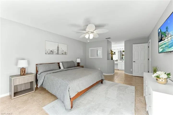 Bedroom with light tile patterned floors, ceiling fan, and ensuite bath
