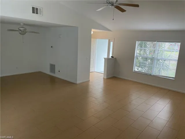 Empty room with a ceiling fan, vaulted ceiling, and baseboards