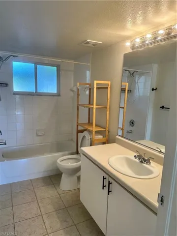 Bathroom with vanity, bathtub / shower combination, a textured ceiling, a textured wall, and light tile patterned flooring