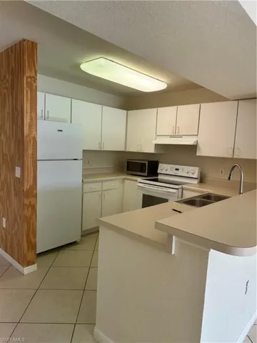Kitchen featuring a peninsula, white range oven, fridge, light countertops, and white cabinetry