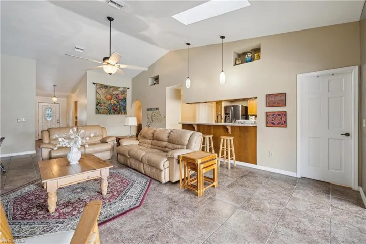 Living room featuring tile flooring, high vaulted ceiling, sink, ceiling fan, and a skylight