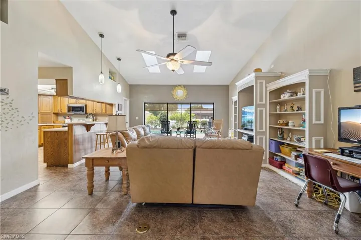 Living room featuring tile floors, high vaulted ceiling, ceiling fan, and a skylight