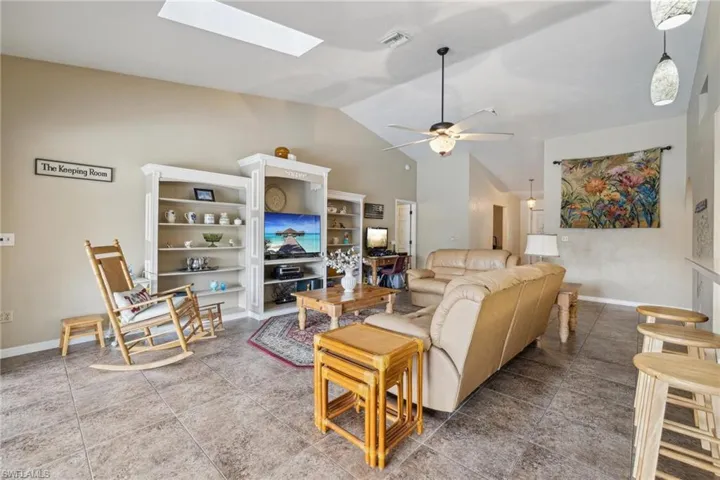 Tiled living room featuring ceiling fan and lofted ceiling with skylight